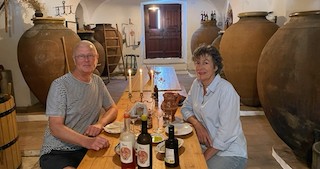 Twee mensen aan een tafel met flessen wijn in een ruimte met grote aardewerken vaten